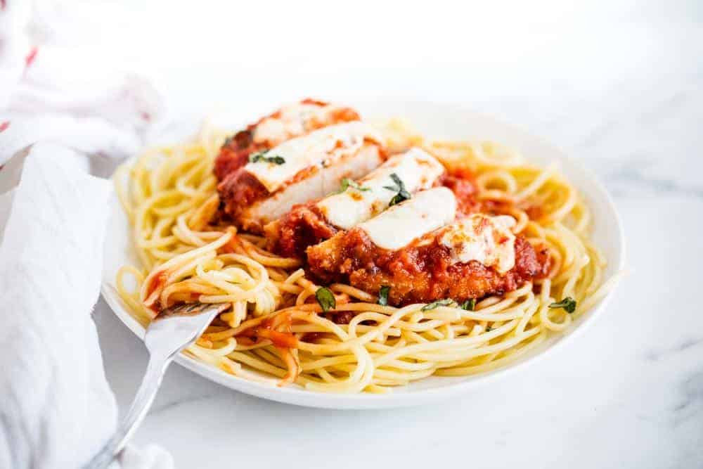 Sliced chicken parmesan served over spaghetti noodles.