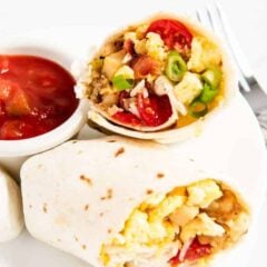 Easy breakfast burrito cut in half showing eggs, bacon and potato filling served on a white plate with a side of salsa.