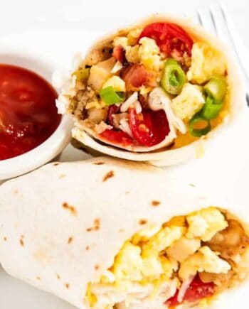 Easy breakfast burrito cut in half showing eggs, bacon and potato filling served on a white plate with a side of salsa.