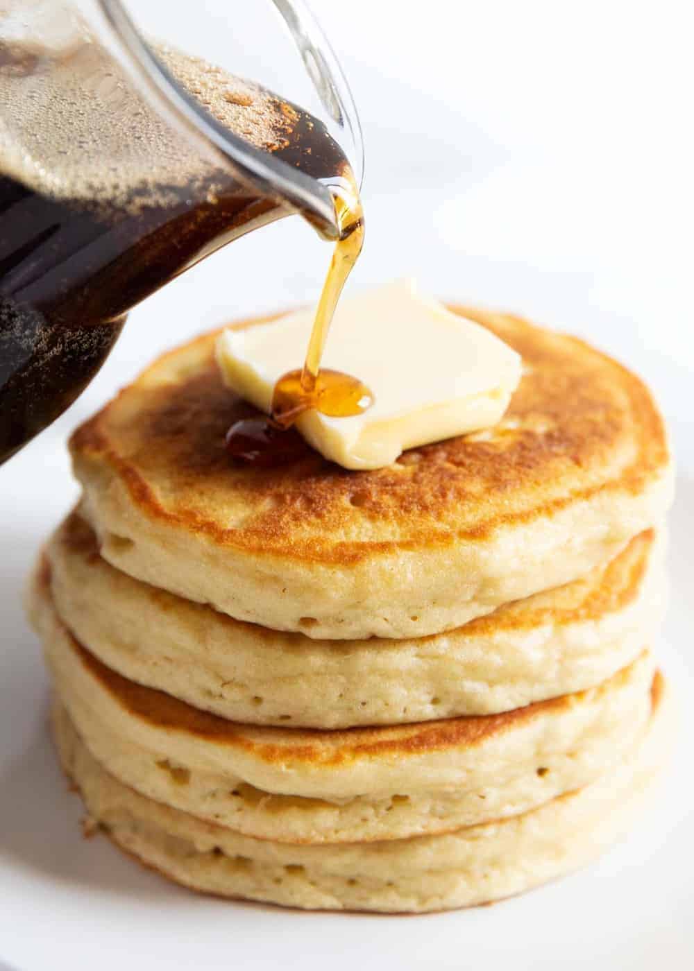 Pancake syrup being poured over a stack of pancakes.