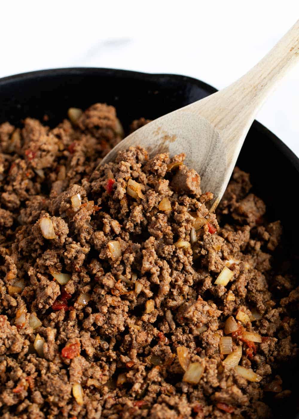 Taco meat in pan with wooden spoon.