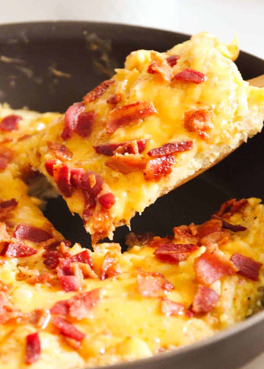 Breakfast skillet in a skillet with a wooden spoon lifting it from the pan.