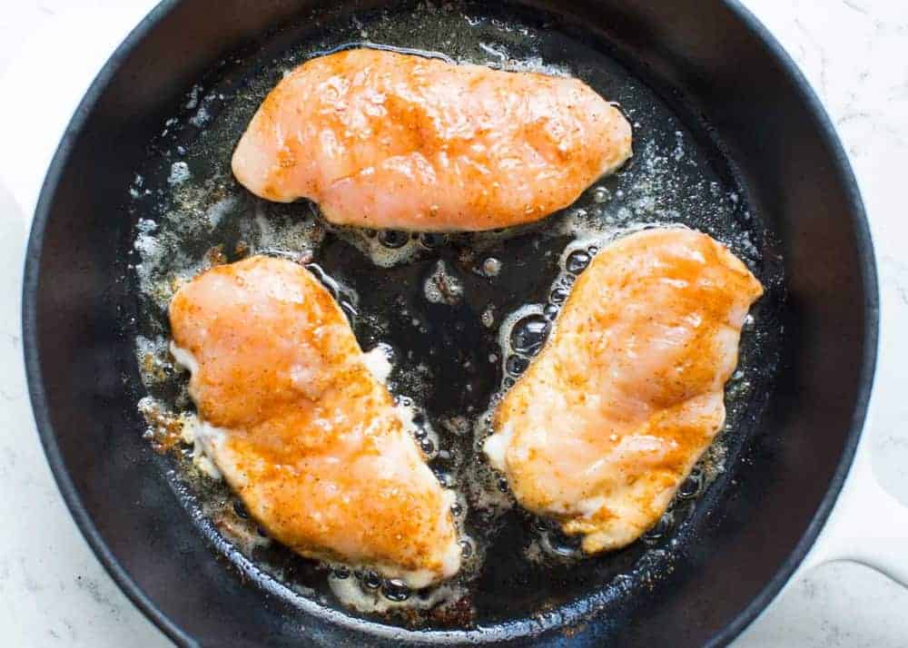 Cooking seasoned chicken breasts in skillet.