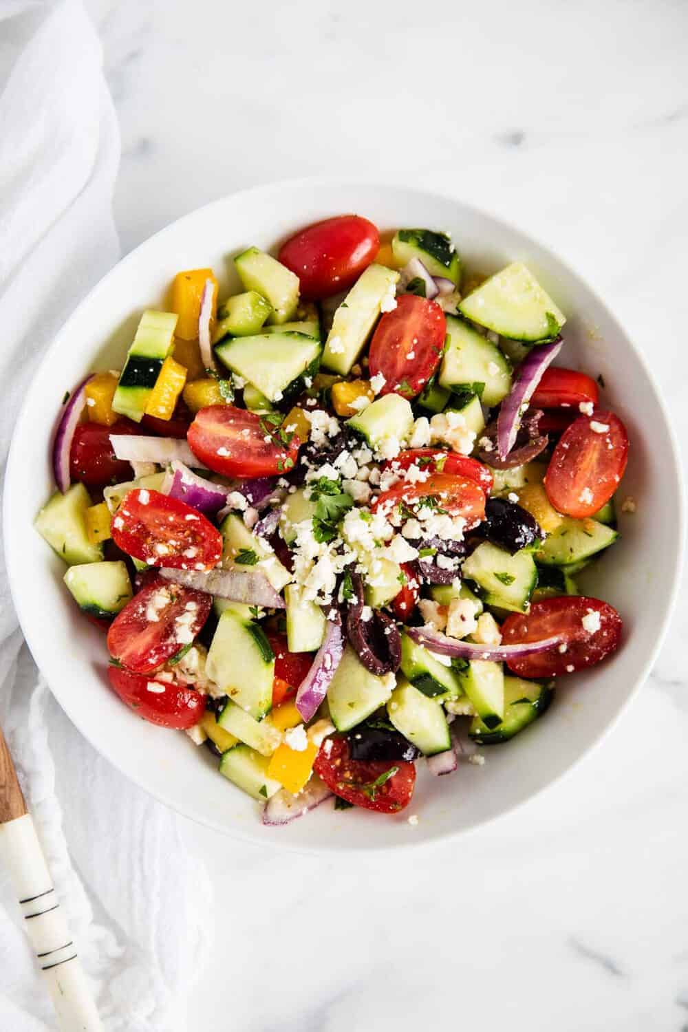 Greek salad in a white bowl on a marble counter top.