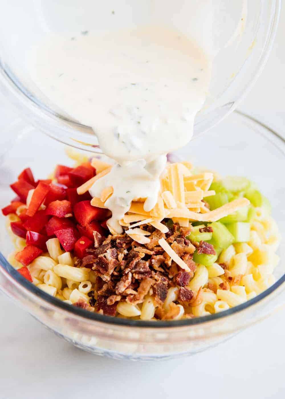 Pouring dressing over macaroni salad ingredients.
