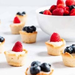 Mini fruit tarts on the counter filled with custard topped with fresh berries.