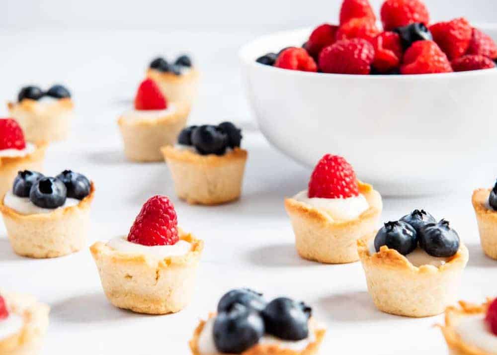 Delicious mini fruit tarts made with a buttery shortbread crust, creamy vanilla custard and topped with fresh fruit. The perfect bite-sized sweet treat for spring and summer! Mini fruit tarts on counter.