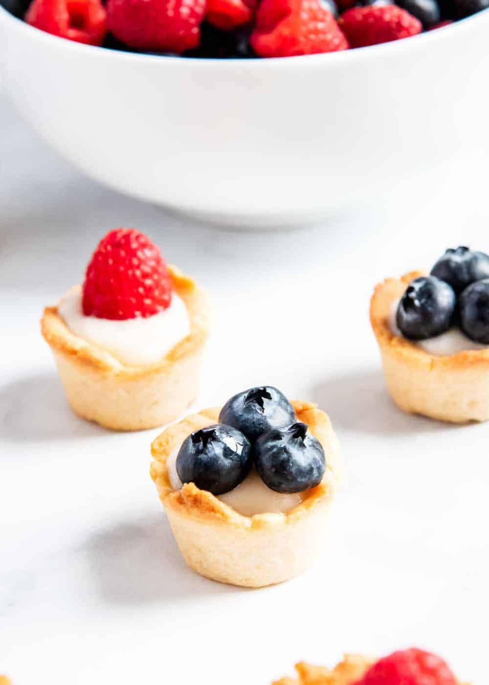 Mini fruit tarts with custard on counter.