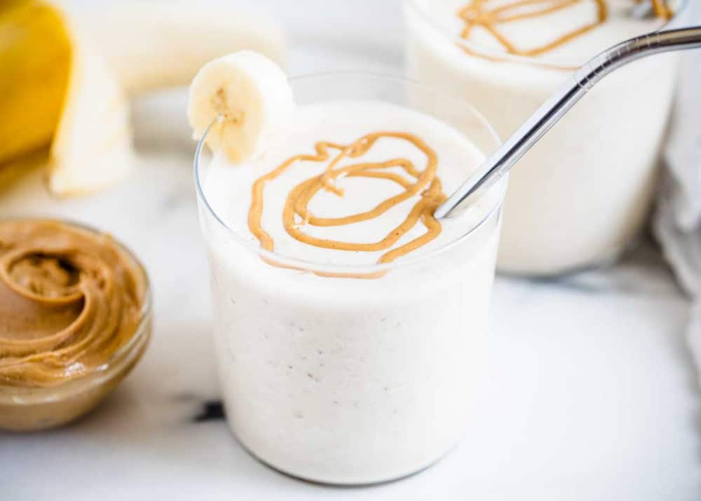peanut butter banana smoothie in a glass with a silver straw 