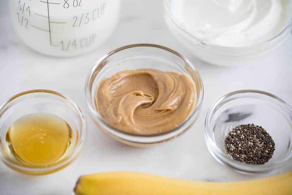 Ingredients in small glass bowls for peanut butter banana smoothie.