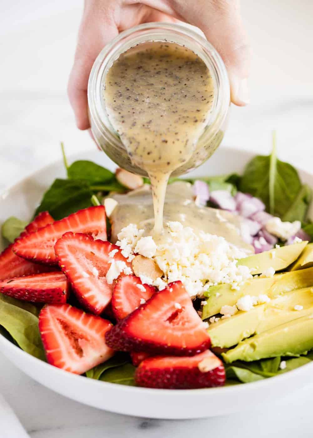 Pouring poppy seed dressing over strawberry spinach salad.