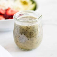 Creamy poppy seed dressing in a jar with a strawberry salad in background.