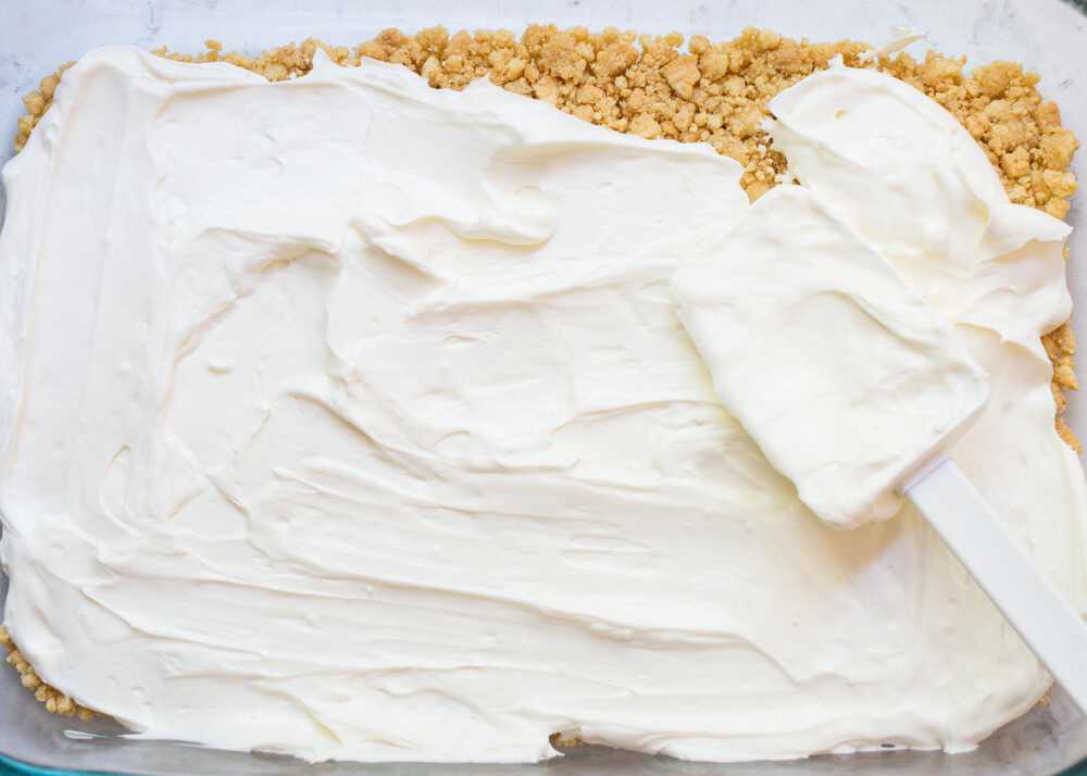 Whipped cream being spread with a spatula onto a golden Oreo crust.