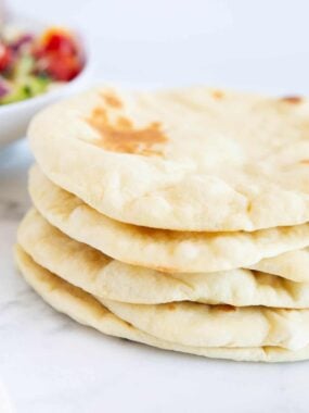 Freshly baked pita bread stacked on the counter showing soft and golden puffy centers.