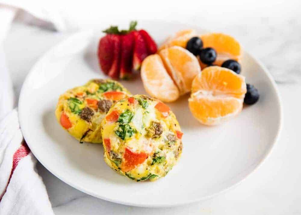 Breakfast egg muffins on white plate with fruit.