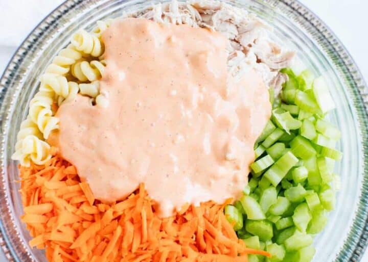 buffalo chicken pasta salad ingredients in a clear bowl with dressing on top