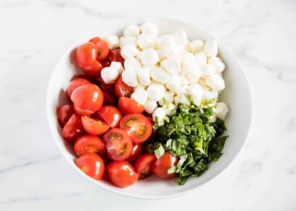 Tomatoes, basil and mozzarella in white bowl.
