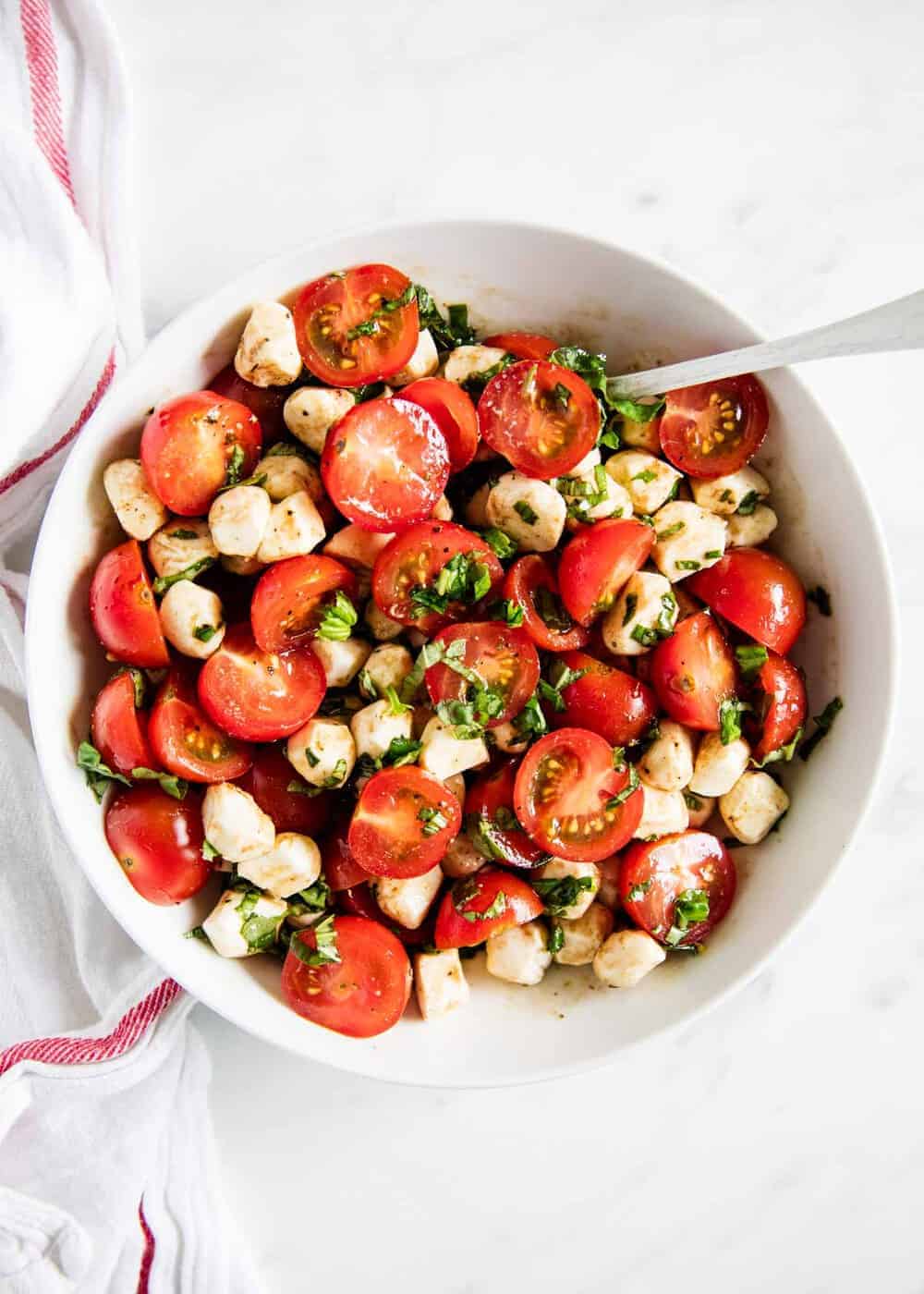 Caprese salad in white bowl with spoon.