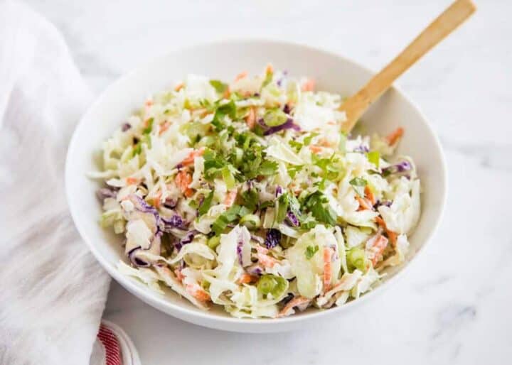 coleslaw in a white bowl with a wooden spoon