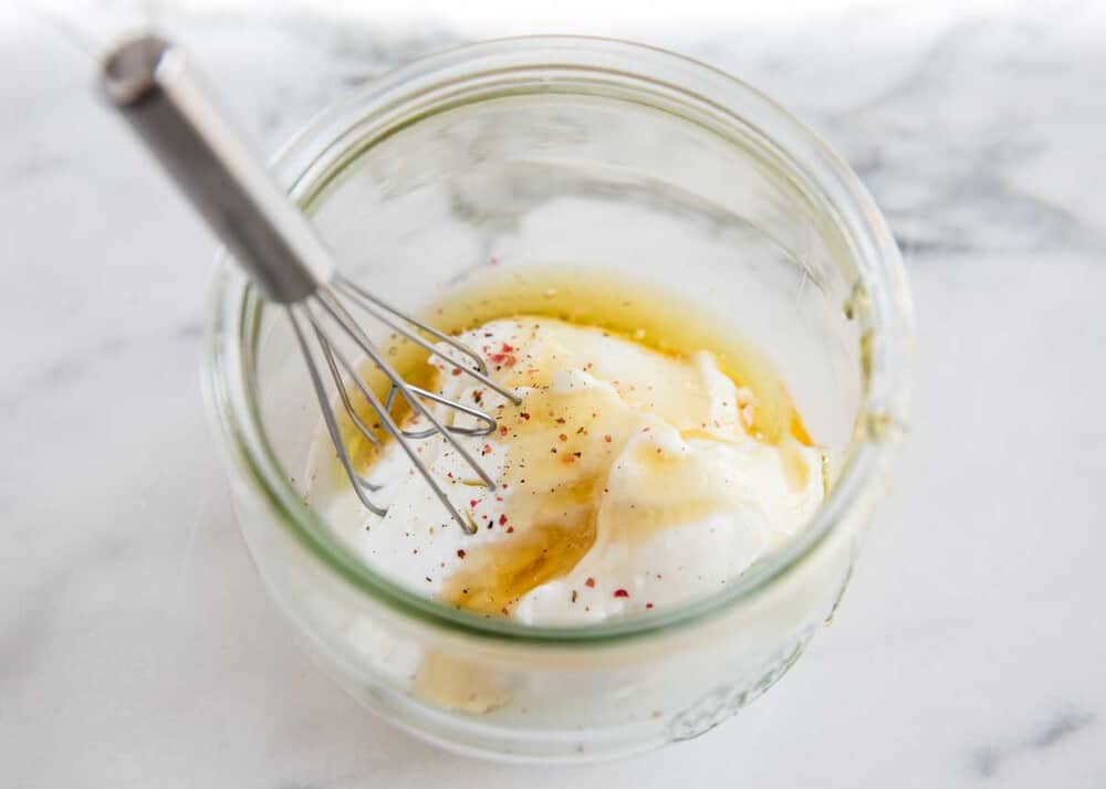 Coleslaw dressing being whisked in a glass bowl.