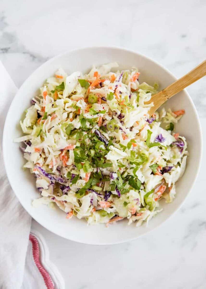 homemade coleslaw in a white bowl with a wooden spoon