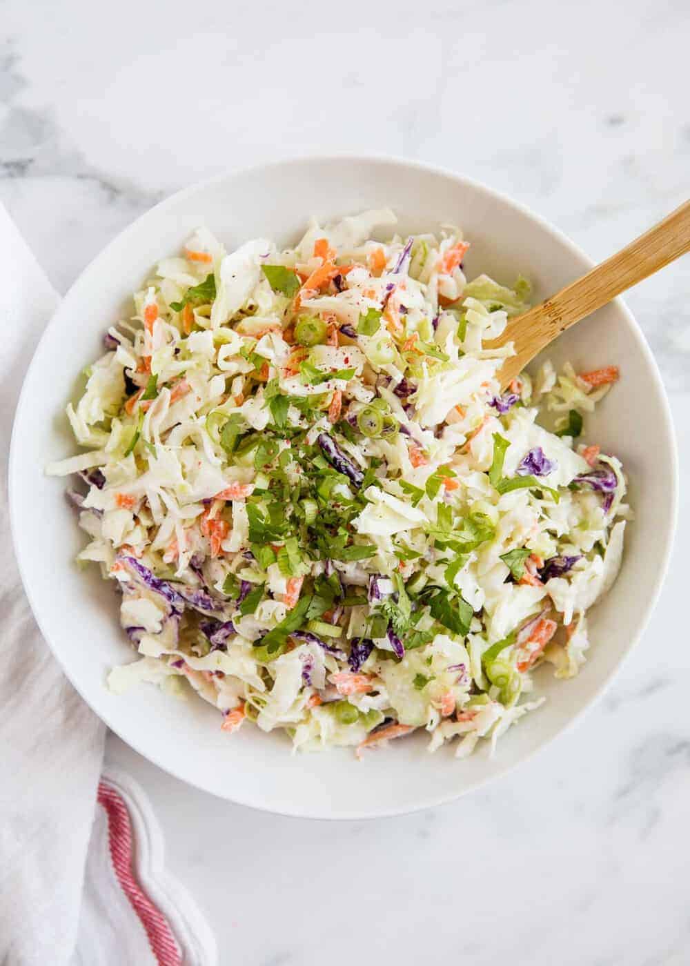 Homemade coleslaw in a white bowl with a wooden spoon.