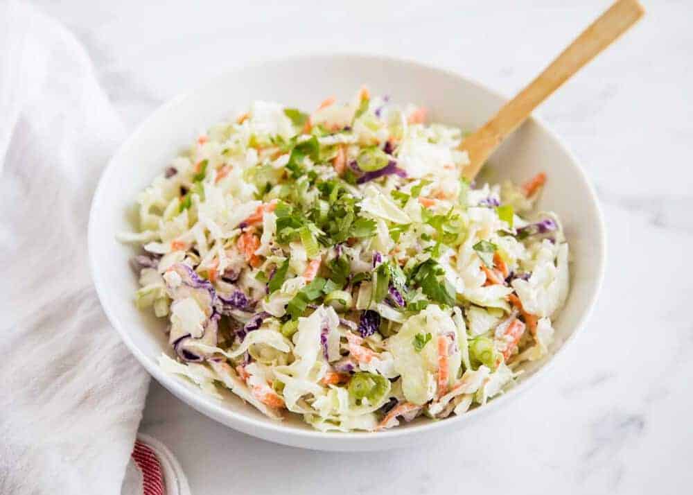 Coleslaw in a white bowl with a wooden spoon.