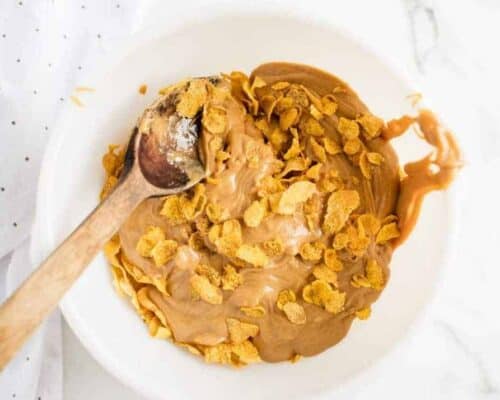 mixing together cornflake cookies in a white bowl with a wooden spoon