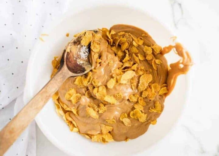 mixing together cornflake cookies in a white bowl with a wooden spoon
