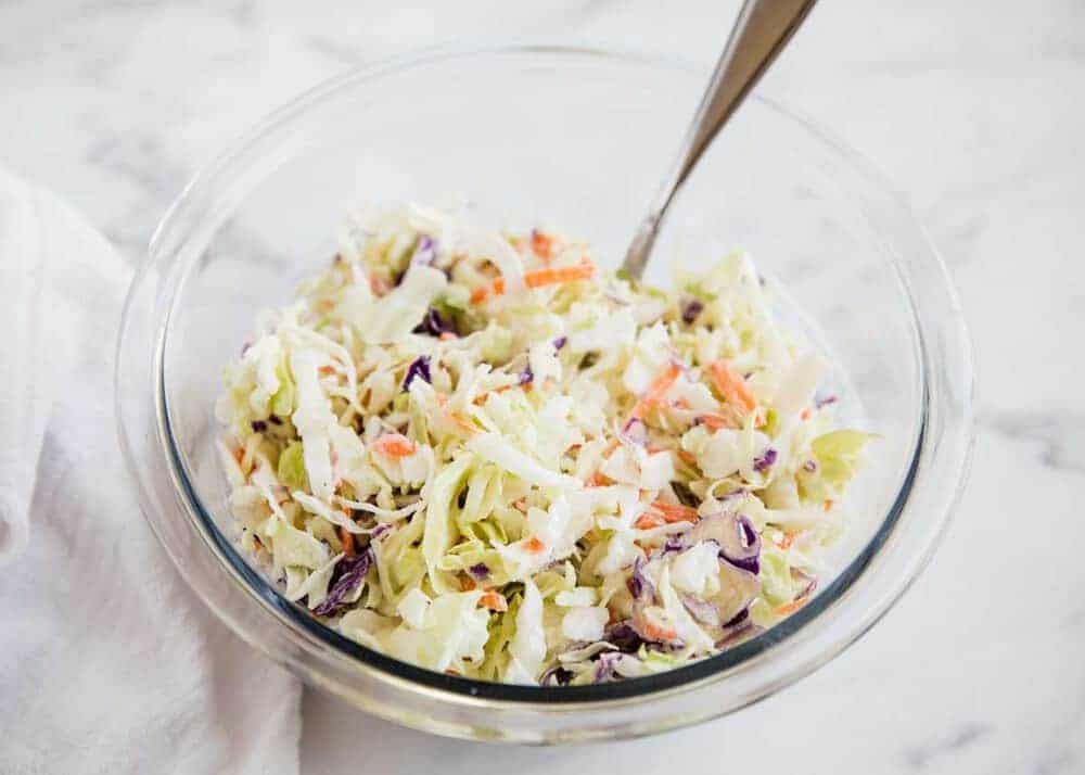 Coleslaw in a glass bowl with a silver spoon.