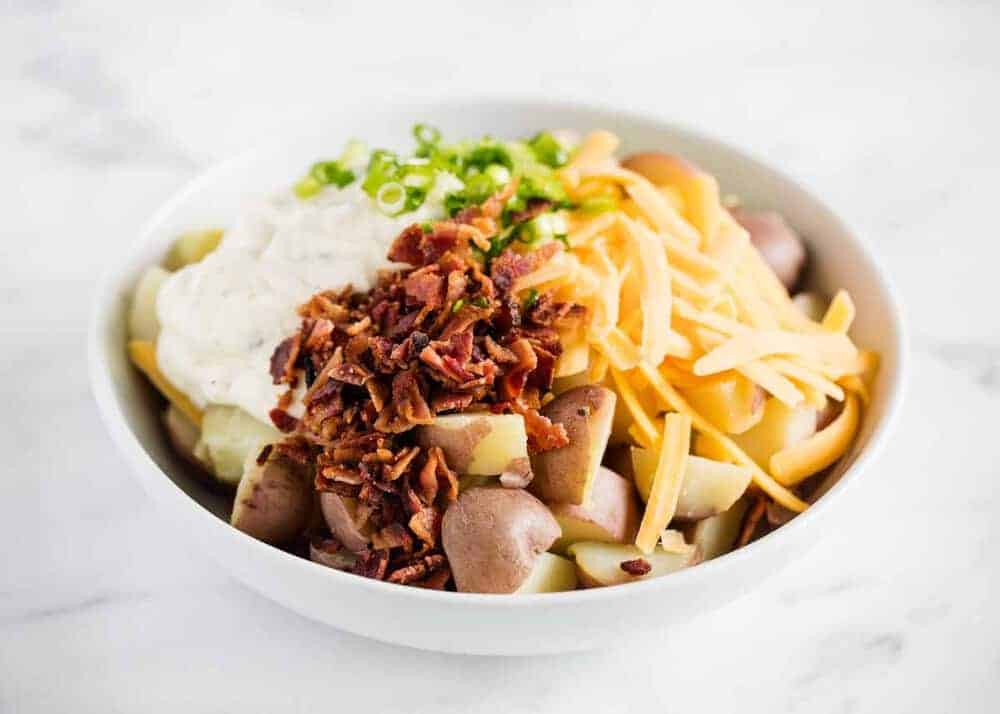 Potatoes, bacon, cheese, green onions, and seasonings in a white bowl.