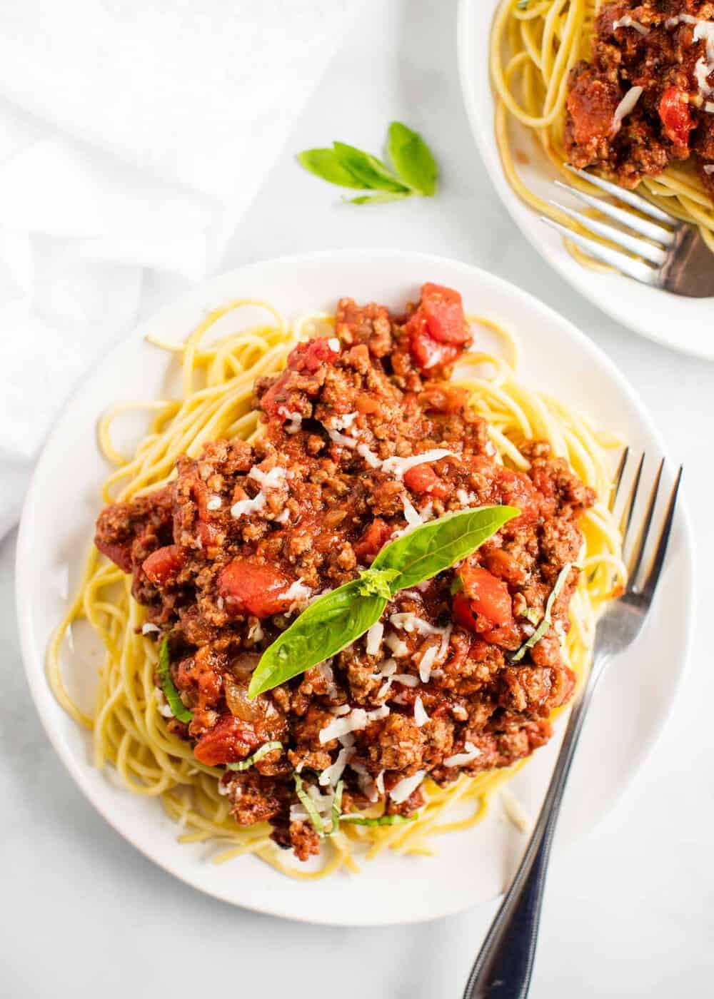 Spaghetti and meat sauce on a white plate topped with basil.