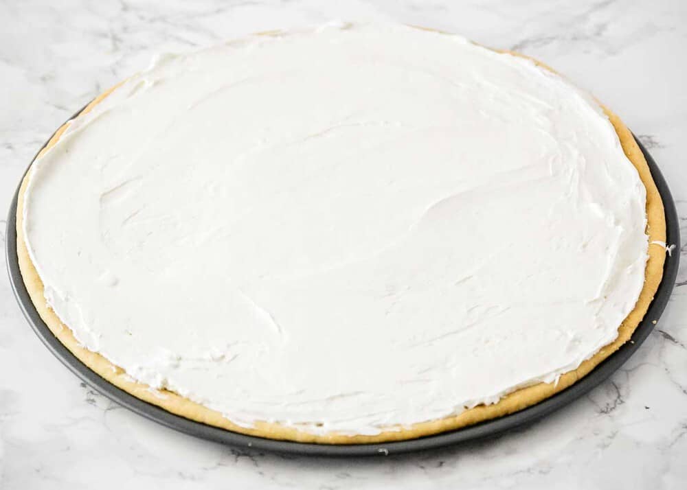 Sugar cookie crust in a pizza pan with cream cheese frosting on top.