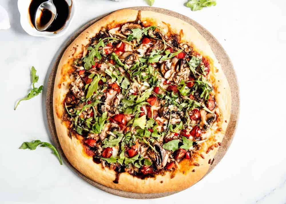 Vegetable pizza on pizza stone topped with arugula and balsamic glaze.