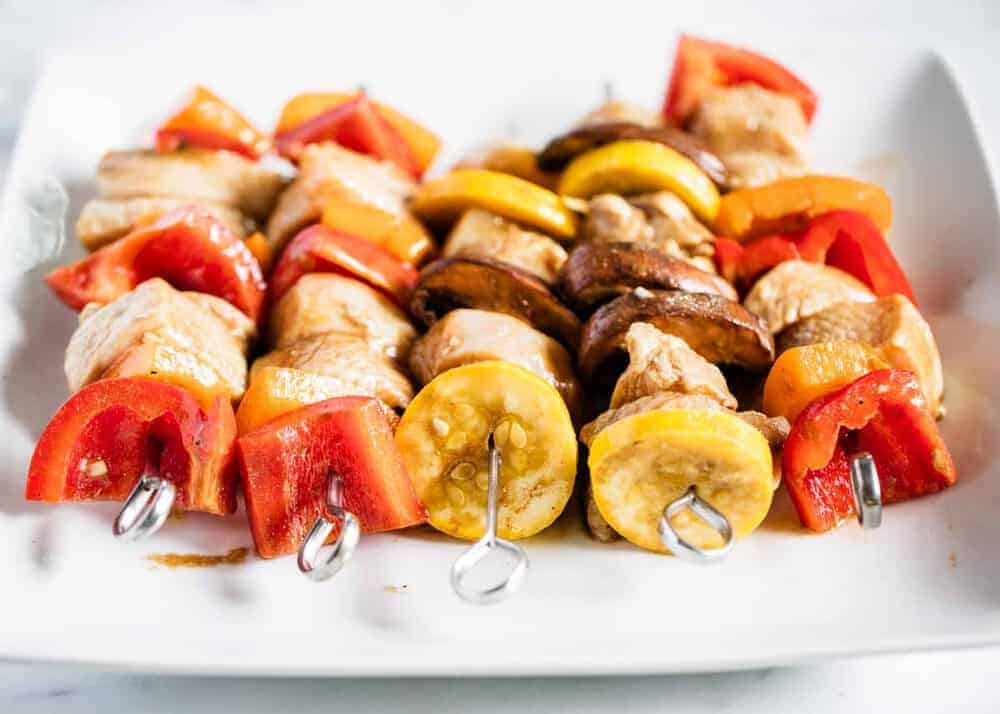 A white plate with chicken kabobs on it. 