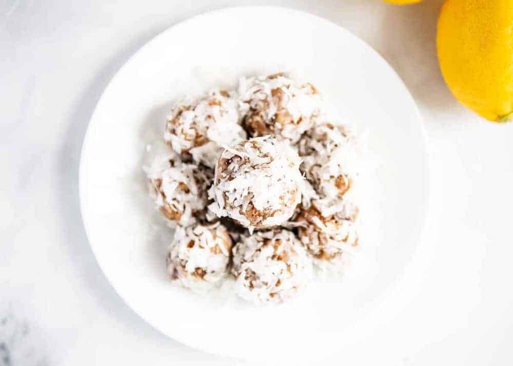 Lemon Coconut Energy Balls - Filled with dates, nuts, coconut, chia seeds and lemon juice. The perfect healthy snack that has no added sugar and is paleo and Whole30 approved! Stack of lemon coconut energy balls on a white plate.