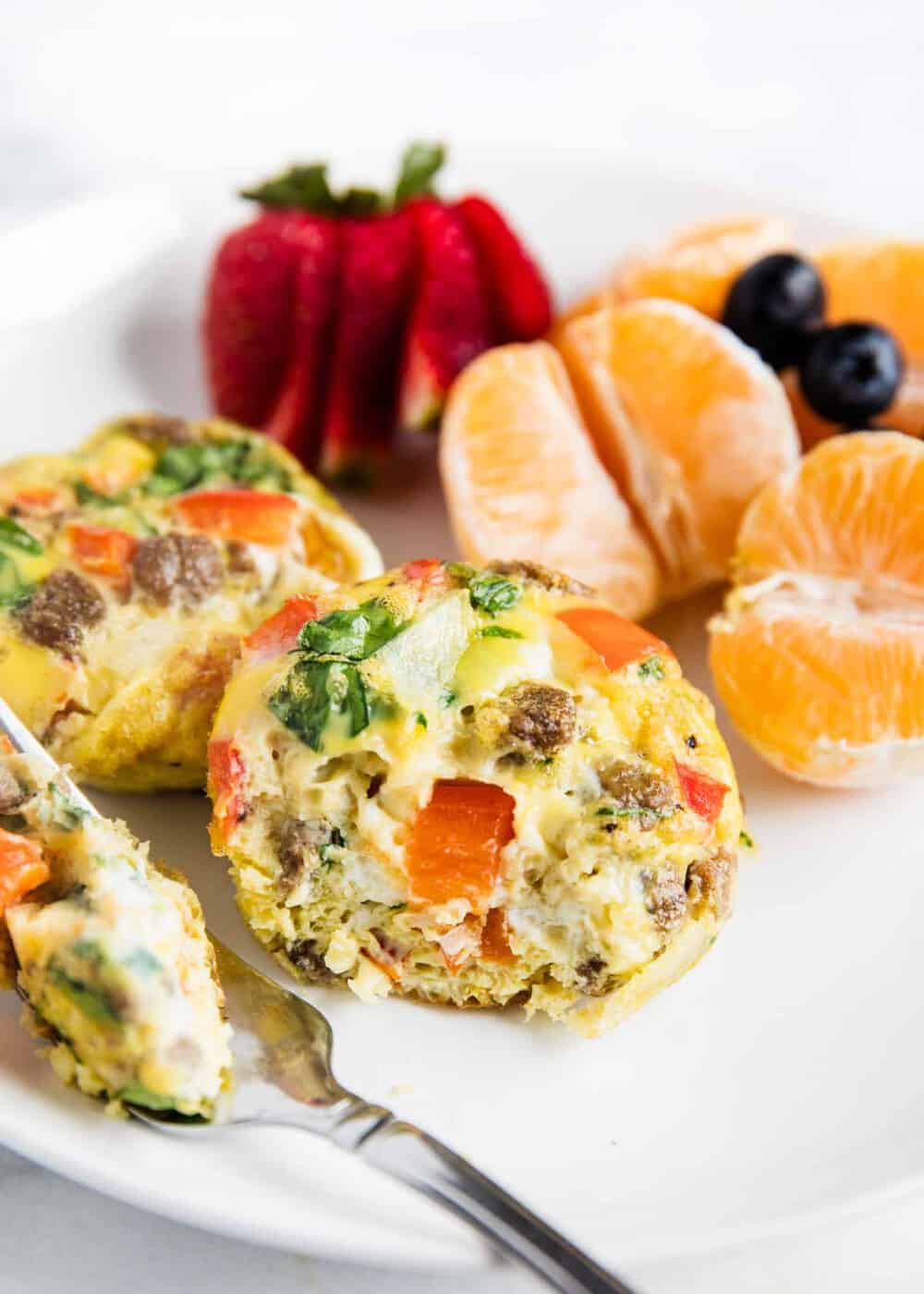 Muffin tin eggs on white plate with fruit.