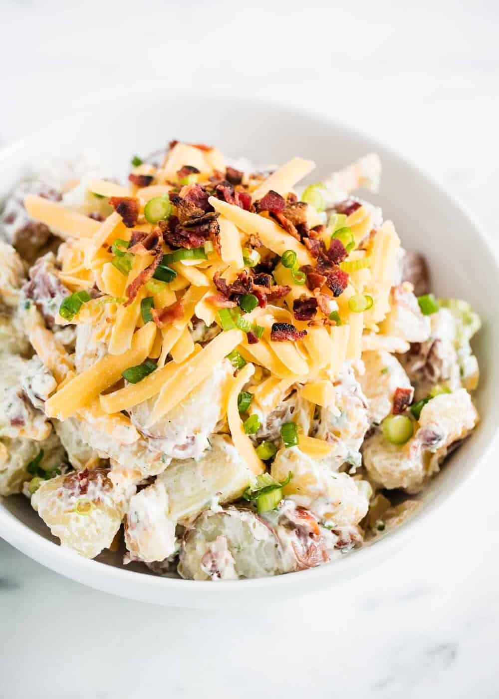 Loaded potato salad with cheese and bacon in a white bowl.