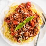 spaghetti and meat sauce with basil on a white plate