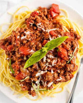 spaghetti and meat sauce with basil on a white plate