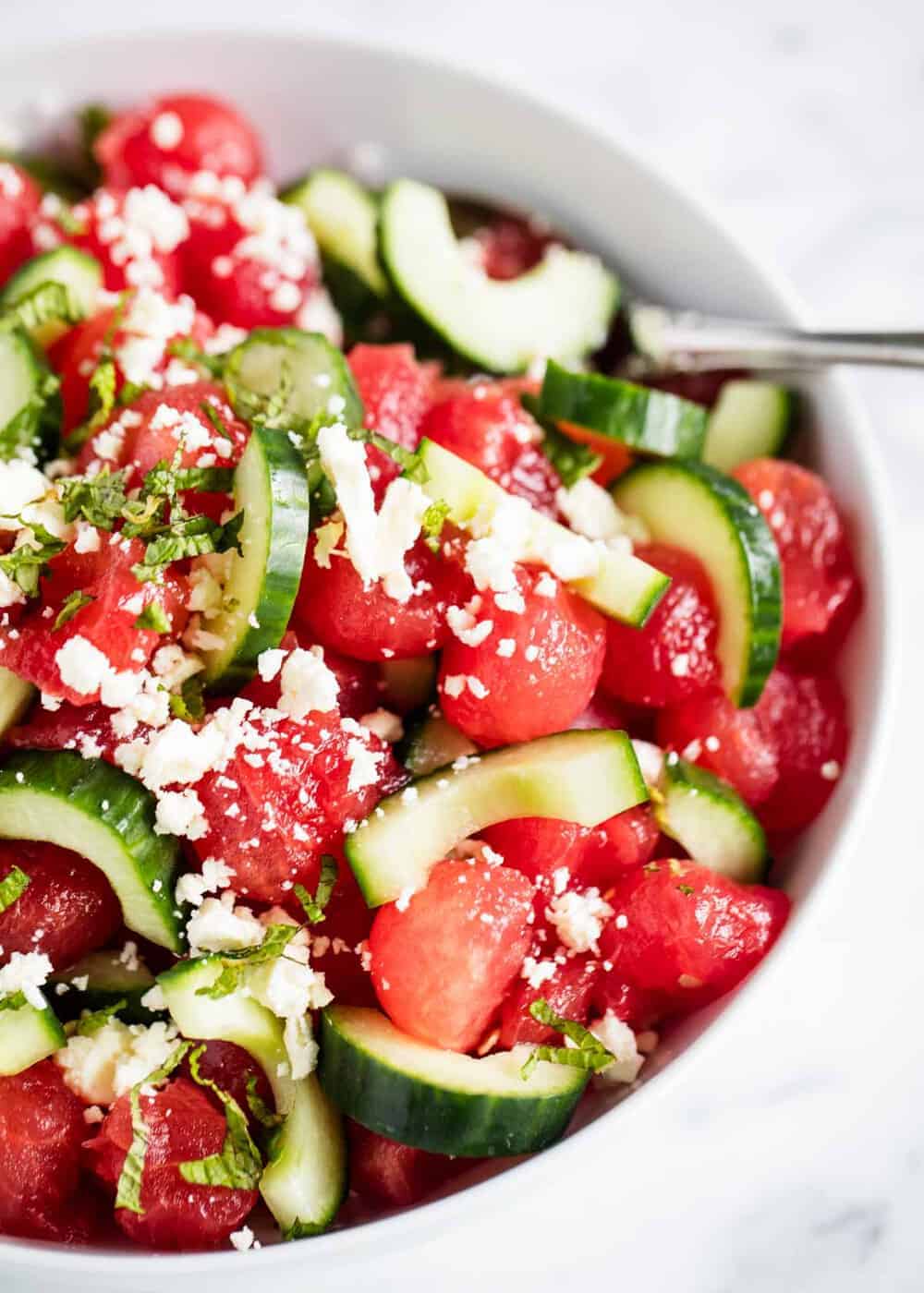 Watermelon salad with cucumber in white bowl.