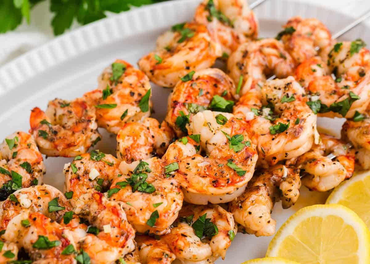 Grilled shrimp skewers on a white plate with sliced lemon.
