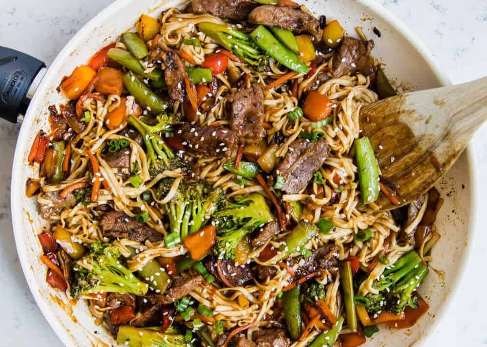 Beef ramen in a white pan with a wooden spoon.