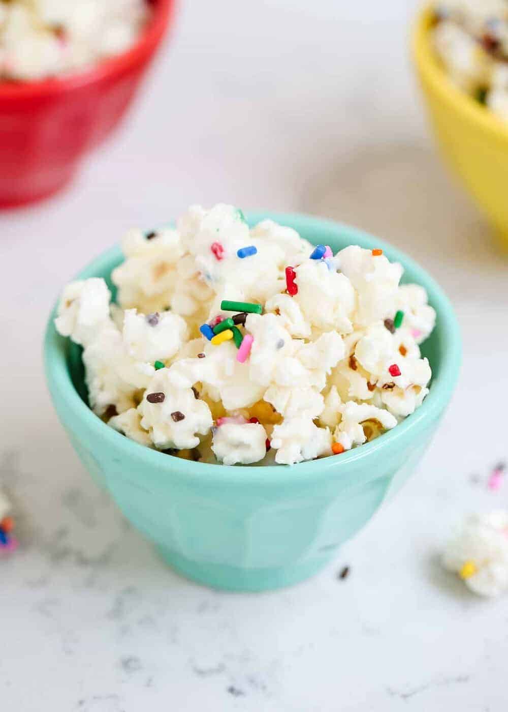 Birthday cake popcorn with sprinkles in a blue bowl.
