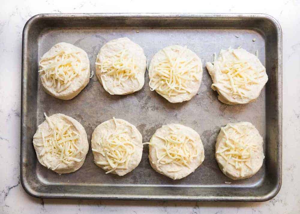 Garlic rolls with shredded cheese on top on a baking sheet.