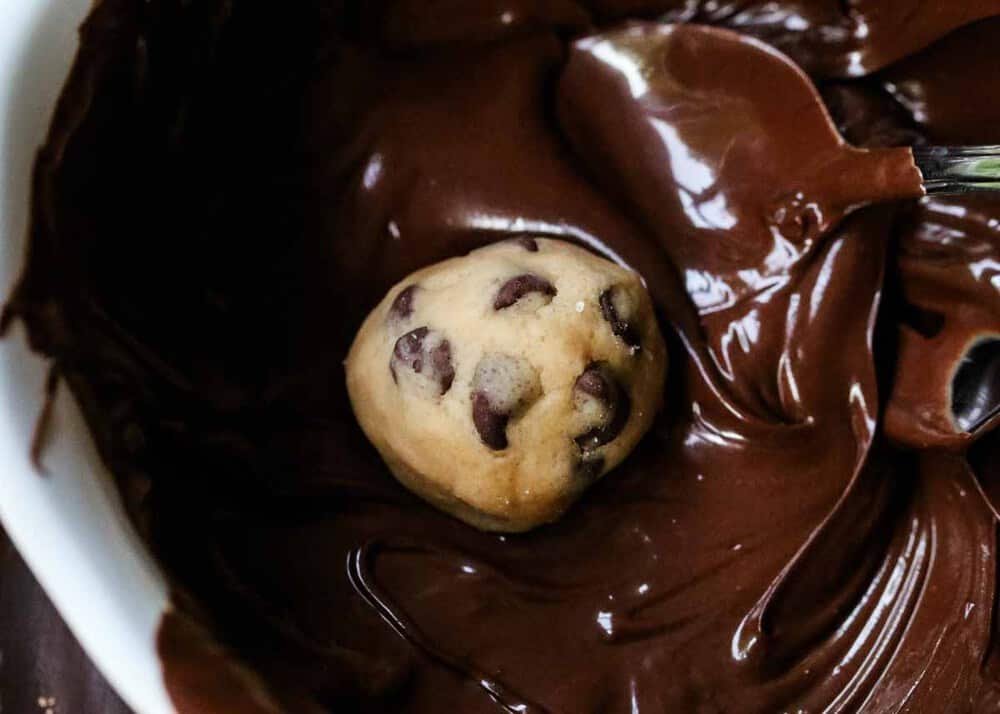 Cookie dough ball in bowl of melted chocolate.