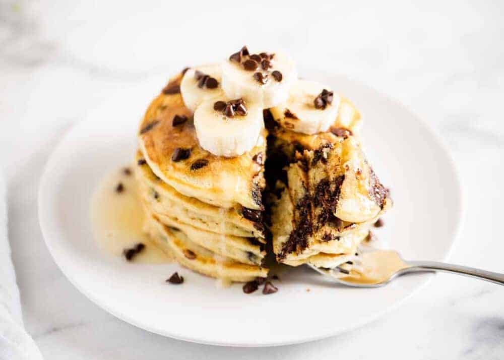 stack of chocolate chip pancakes on a plate topped with sliced bananas 