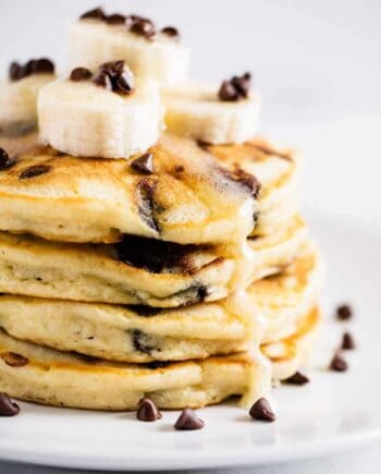 stack of chocolate chip pancakes with sliced bananas and syrup on top