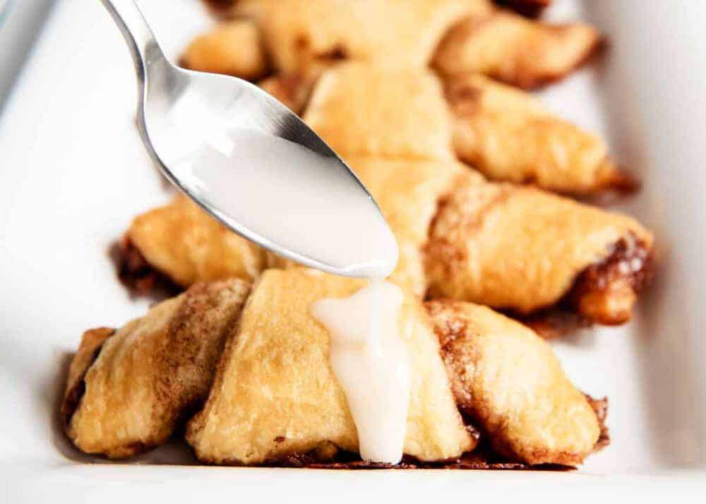 drizzling glaze on top of cinnamon crescent rolls with a spoon