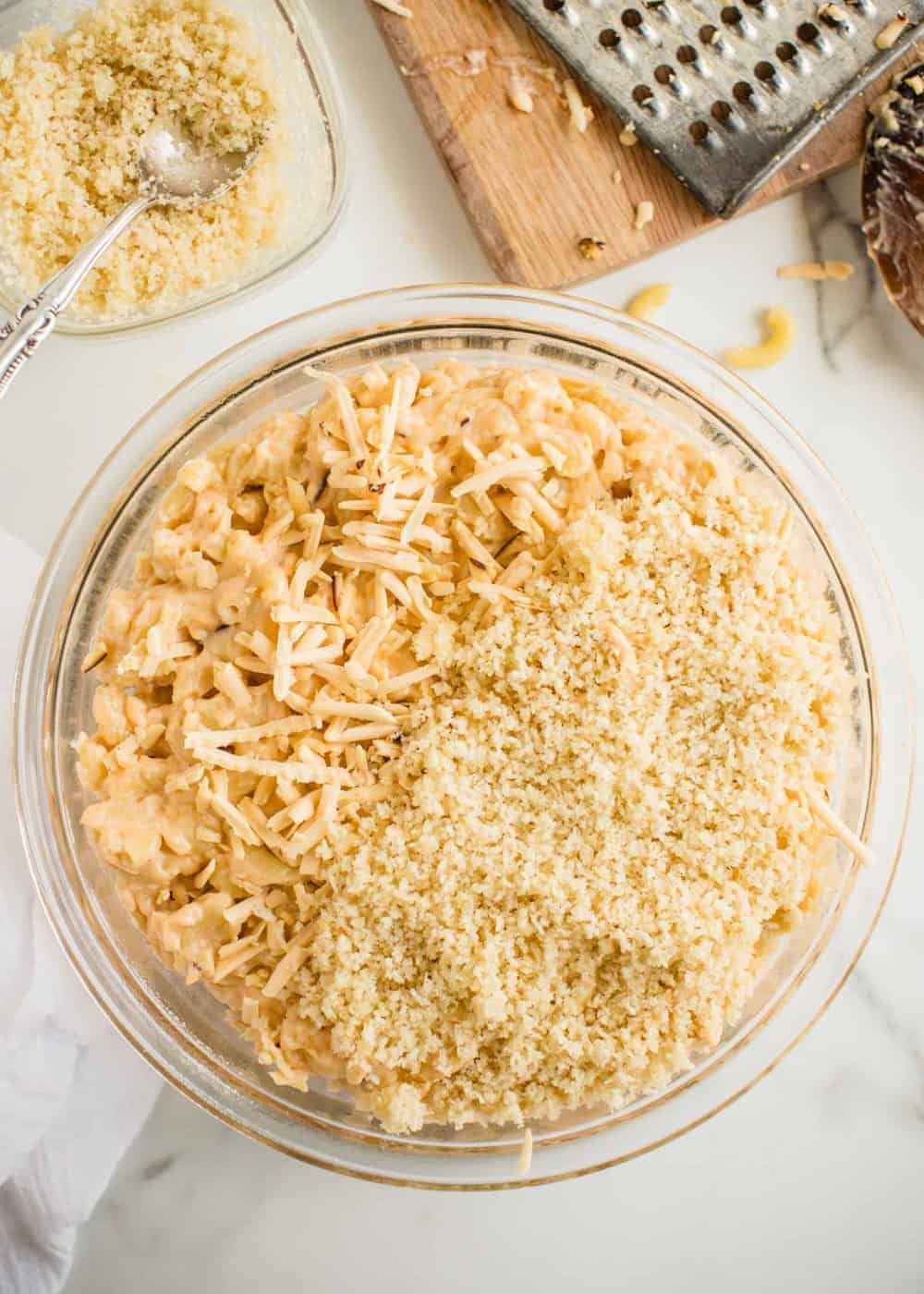 mixing together shredded gouda, breadcrumbs and mac n cheese in a glass bowl